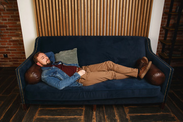 Beautiful elegant fashionable young man in a blue jacket sits on sofa