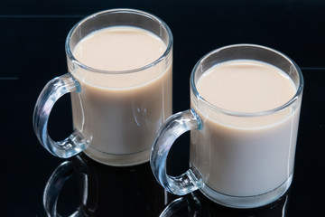 Two glass cups with tea with milk on a smooth dark surface