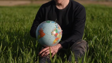 man spinning earth globe sitting in green field