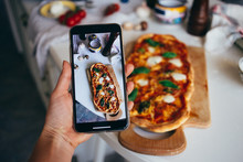 Selective Focus On Smartphone, Person Makes Photo Of Fresh Baked Homemade Pizza At Home. Learn New Skills And Hobby During Lockdown. Sour Dough Pizza For Bored Hipsters