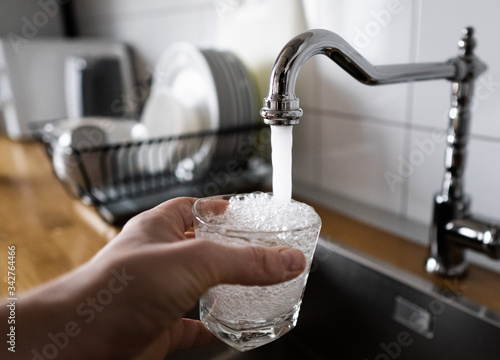 man filling a glass of water from a stainless steel kitchen tap. male\'s hand pouring water into the glass from chrome faucet to drink running water with air bubbles. potable water and safe to drink.