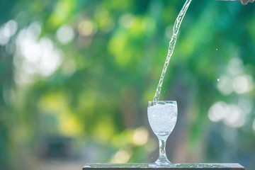 Water splash in glass Select focus blurred background.Drink water pouring in to glass over sunlight and natural green background.Nature conservation concept.