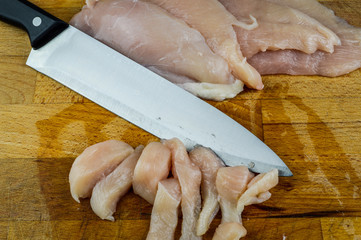 Chopped raw chicken breasts and knife on a wooden chopping board