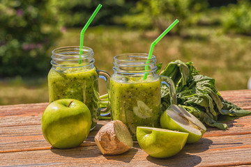 Wall Mural - Healthy Vegan Green Smoothie With Spinach, apple, celery, kiwi, Brussels sprout, avocado, in glass jars, outdoor, over nature background.