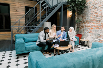 Successful four young international business people working together in office. Caucasian lady brainstorming with their team business colleagues, talking about new ideas, using laptop