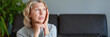 © JENOCHE - Mature woman sitting on a white sofa in a home touching her head with her hands while having a headache pain and feeling unwell