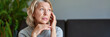 © JENOCHE - Mature woman sitting on a white sofa in a home touching her head with her hands while having a headache pain