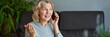 © JENOCHE - Happy mature woman using mobile phone while sitting on sofa at home