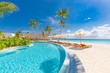 © icemanphotos - Outdoor tourism landscape. Luxurious beach resort with swimming pool and beach chairs or loungers under umbrellas with palm trees and blue sky. Summer travel and vacation background concept