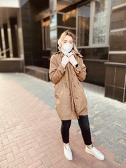 girl in a protective mask closed her eyes about fear. Stylish young women in a flu mask and protective gloves against coronavirus walks on the street and looks away. Covid-19.