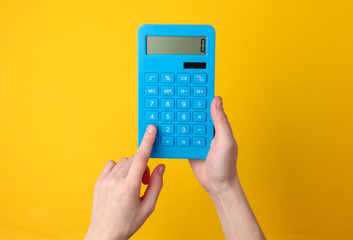 Hand holds blue calculator on yellow background.