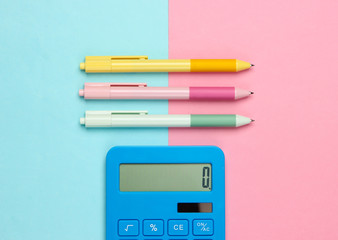 Wall Mural - Blue calculator with colored pens on a pink blue pastel background. Top view. Office tools. Economist