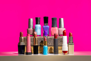 Various makeup items, lipstick and nail polish. Mixed colors against a modern bright pink background.