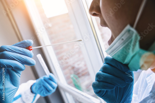 Fotografía Medical in protective clothing takes COVID-19 swab test tube from mouth at Covid-19 test center during coronavirus epidemic
