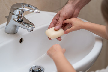 Wall Mural - Father is washing hands of his baby toddler, rubbing with soap for corona virus prevention, hygiene to stop spreading coronavirus. Concept of teaching and learning healthy habits from an early age.