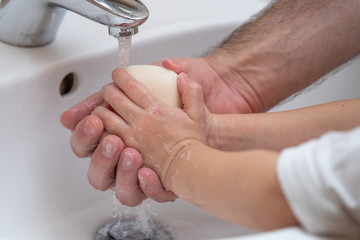 Father is washing hands of his baby toddler, rubbing with soap for corona virus prevention, hygiene to stop spreading coronavirus. Concept of teaching and learning healthy habits from an early age.