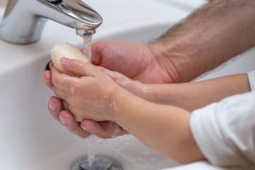 Wall Mural - Father is washing hands of his baby toddler, rubbing with soap for corona virus prevention, hygiene to stop spreading coronavirus. Concept of teaching and learning healthy habits from an early age.