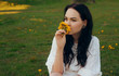 © MoreThanProd - Gorgeous brunette sits in a park on the grass in a white dress and holds dandelions, yellow flowers dandelions.  a background of a field with flowers. The girl is no longer allergic.