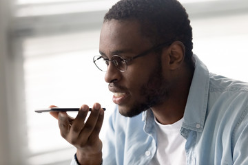 African american businessman talking for sound message recording. Smiling diverse man using smartphone online media service for network social communication.