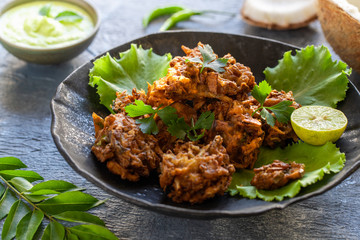 Indian cuisine Indian food. pakora traditional Indian deep-fried snack. pakoras on black plate with coconut chutney sauce curry leaves. national appetiser authentic vegetarian Asian food. travel food