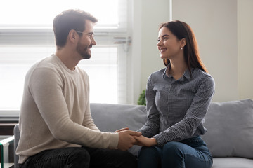 Happy young man holding attractive woman hands on couch. Smiling romantic couple enjoy time together. Beautiful family have fun time and enjoy romantic pastime.