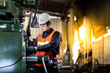 Mechanical Engineering control lathe machine in factory facility. Safety First at work place. Man Worker at industrial factory wearing uniform and hardhats.