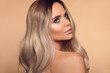 © Victoria Andreas - Ombre blond wavy hairstyle. Beauty fashion blonde woman portrait. Beautiful girl model with makeup, long healthy hair style posing isolated on studio beige background.