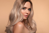 Ombre blond wavy hairstyle. Beauty fashion blonde woman portrait. Beautiful girl model with makeup, long healthy hair style posing isolated on studio beige background.