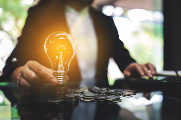 Wall Mural - businesswoman putting a light bulb over coins stack on the table while calculating for saving energy