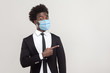 © khosrork - Portrait of funny young handsome worker man wearing black suit with surgical medical mask standing showing and pointing at empty background copyspace. indoor studio shot isolated on gray background.