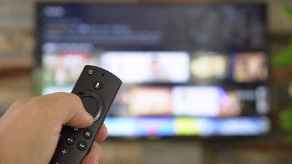 Male hand holding the TV remote control and changing TV channels