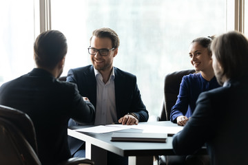 Wall Mural - Two confident businessmen shaking hands on group negotiations, business partners greeting each other, celebrating making good successful deal, signing contract, sitting at table in boardroom