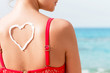 © sosiukin - Beautiful girl in red swimsuit has sunblock in shape of heart at the back at the beach