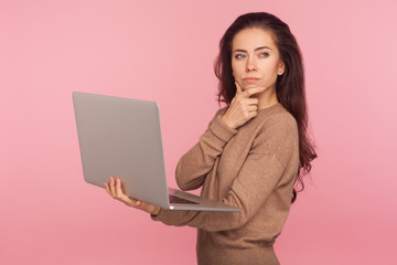 Wall Mural - Inspiration, business idea. Portrait of young woman in casual sweater holding laptop and thinking over startup strategy with serious doubtful expression. indoor studio shot isolated on pink background