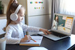 © ty - Smart small preschooler girl in headphones watch online lesson and communicate with teacher at home, little child in earphones study on Internet using laptop wireless connection.