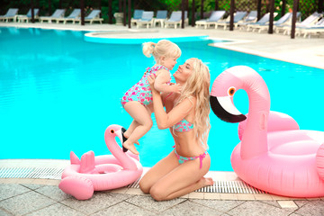 Wall Mural - Family look. Beautiful mother having fun with daughter. Happy summer vacations.  Blonde pretty woman with her little girl wear in fashion same swimwears playing by pink Inflatable pool float flamingo.