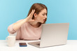© khosrork - I can't hear, Woman holding arm near ear trying to listen secret talk on video call on laptop, bad internet connection, online conference from home office. indoor studio shot isolated, blue background