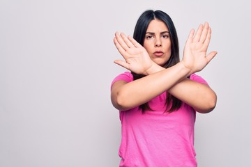 Poster - Young beautiful brunette woman wearing casual pink t-shirt standing over white background Rejection expression crossing arms doing negative sign, angry face