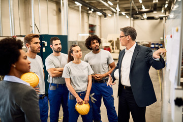 Company manager presenting business strategy to group of workers in a factory.