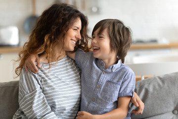 head shot happy young woman cuddling talking to small kid son, having fun together on couch in studi