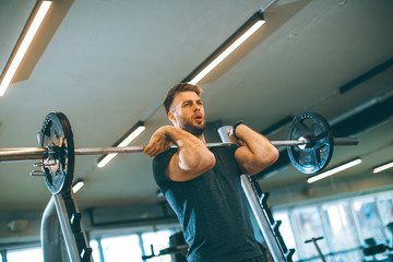 Wall Mural - Young man working out with barbells in the gym