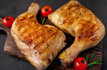 two grilled chicken legs with spices on a cutting board on a stone background