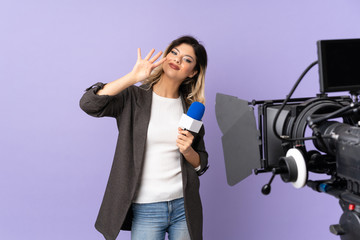 Reporter teenager girl holding a microphone and reporting news isolated on purple background happy and counting four with fingers