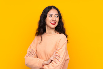 Wall Mural - Spanish Chinese woman over isolated yellow background with arms crossed and happy