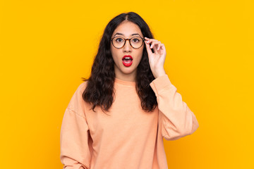 Spanish Chinese woman over isolated yellow background with glasses and surprised