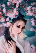 Woman Fashion Close-up Portrait. Beautiful Mixed Race Asian Caucasian Young Girl Perfect Skin Art Make-up Oriental Eye Shape Natural Cosmetics. Trendy White Japanese Kimono Long Black Hair Flower Tree