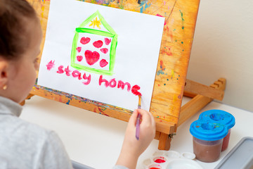 Wall Mural - Child writes words Stay Home with red watercolor under painted house with hearts on the easel. Stay Home concept.