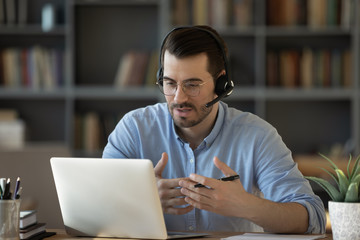 Wall Mural - confident man teacher coach wearing headset speaking, holding online lesson, focused student wearing