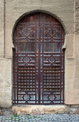 Wall Mural - Medieval horseshoe arch with a wooden brown door ornated with rusty rivets of a religious christian church with islamic shapes and forms decoration