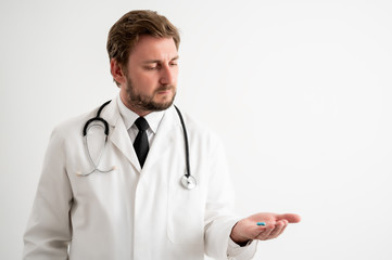 Male doctor with stethoscope in medical uniform showing blue pills